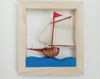 Può includere: Un piccolo veliero di legno con una vela bianca e una bandiera rossa, che galleggia su onde blu, incorniciato in una cornice di legno naturale.
