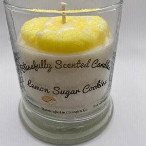 Peut inclure: Une bougie en verre transparent avec une cire parfum&eacute;e au citron et aux biscuits au sucre. Le pot est dot&eacute; d'une &eacute;tiquette blanche avec le texte "Blissfully Scented Candles Lemon Sugar Cookies 9 oz Handcrafted in Covington Ga."