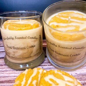Peut inclure: Deux pots en verre de bougies parfum&eacute;es au cookie &agrave; l'avoine glac&eacute;. Les bougies sont surmont&eacute;es d'une couche de cire de couleur vanille qui ressemble &agrave; du gla&ccedil;age sur un cookie. Les pots sont pos&eacute;s sur une surface en bois avec deux cookies &agrave; l'avoine glac&eacute;s.