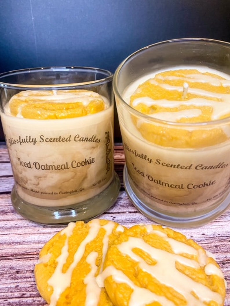 Peut inclure: Deux pots en verre de bougies parfum&eacute;es au cookie &agrave; l'avoine glac&eacute;. Les bougies sont surmont&eacute;es d'une couche de cire de couleur vanille qui ressemble &agrave; du gla&ccedil;age sur un cookie. Les pots sont pos&eacute;s sur une surface en bois avec deux cookies &agrave; l'avoine glac&eacute;s.