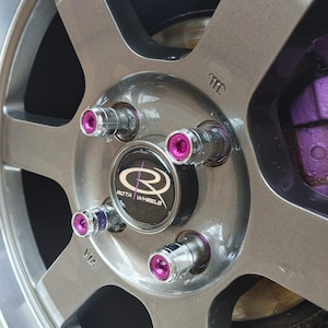 May include: Close-up of a silver car wheel with a black centre cap that says "Rota Wheels". The wheel has five spokes and purple lug nuts.