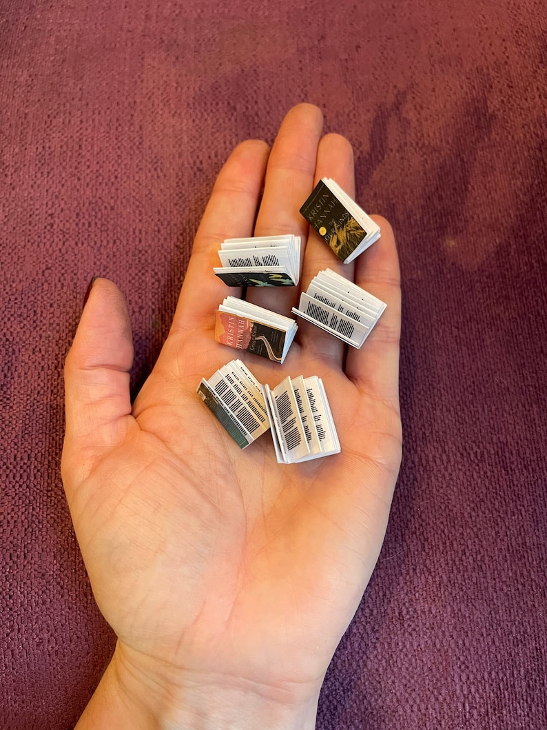 K&ouml;nnte beinhalten: Eine Hand h&auml;lt eine Sammlung von Miniaturb&uuml;chern. Die B&uuml;cher sind geschlossen und haben verschiedene Titel und Umschl&auml;ge.