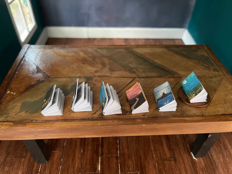 K&ouml;nnte beinhalten: Eine Reihe von sechs Miniaturb&uuml;chern auf einem Holztisch. Die B&uuml;cher sind alle in verschiedenen Farben und haben verschiedene Titel. Die B&uuml;cher sind in einer Reihe von links nach rechts angeordnet.