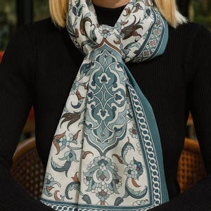 Könnte beinhalten: Gemusterter Schal mit türkisfarbenem Rand und aufwendigen floralen und geometrischen Designs in Türkis, Braun und Creme. Der Schal ist um den Hals drapiert und zeigt das detaillierte Muster und die Farbpalette. Der Schal ist aus weichem Material.