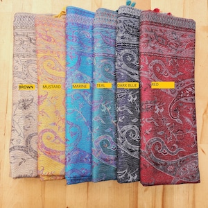 May include: Six patterned scarves in different colours, including brown, mustard, marine, teal, dark blue, and red. The scarves are arranged horizontally on a wooden surface.
