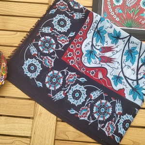Op de afbeelding: Een donkerblauw vierkant van stof met een wit, rood en blauw bloemenpatroon. Het patroon bevat gestileerde bloemen en bladeren.