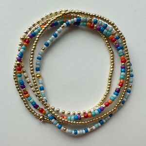 Peut inclure: Un bracelet multi-rangs de perles avec des perles dorées, blanches, bleues, turquoise, violettes et orange.