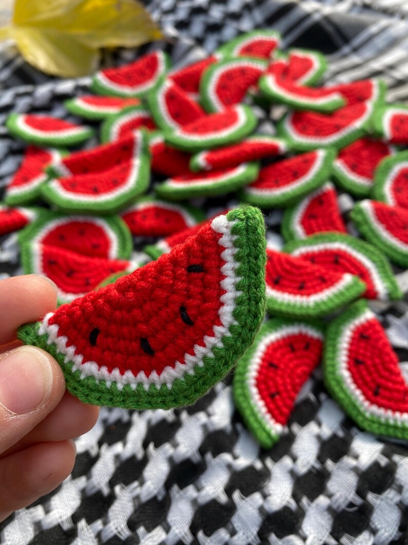May include: A collection of crocheted watermelon slices in red, green and white. The watermelon slices are arranged in a pile on a black and white checked fabric.
