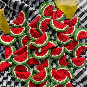 May include: A collection of crocheted watermelon slices in red, green and white. The slices are arranged in a random pattern on a black and white chequered fabric.