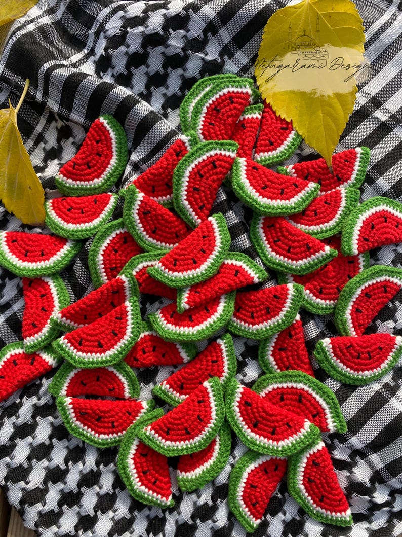 May include: A collection of crocheted watermelon slices in red, green and white. The slices are arranged in a random pattern on a black and white chequered fabric.