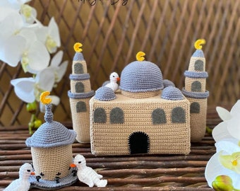 May include: A crocheted mosque with a grey dome and beige walls, two smaller crocheted mosques with grey domes and beige walls, and two white crocheted doves. The mosques have yellow crescent moons on top.