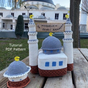Könnte beinhalten: Häkelte Amigurumi-Moschee mit einer blauen Kuppel und weißen Minaretten. Die Moschee steht auf einem Holztisch mit einem Schild, auf dem "Hosgeldin Ya Sehri-i Ramazan" steht.