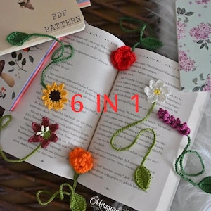 May include: Six crocheted flower bookmarks with green stems and leaves, featuring a red rose, a yellow sunflower, a white daisy, a dark red flower, an orange flower, and a purple sprig, resting on an open book with the text 6 IN 1.