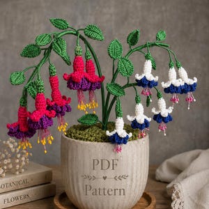 Può includere: Una pianta di fucsia all'uncinetto in un vaso di ceramica grigio chiaro con la scritta PDF Pattern incisa sul davanti. La pianta presenta foglie verdi all'uncinetto e fiori pendenti a forma di campana in magenta con viola e bianco con blu.