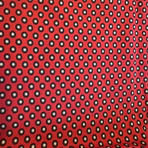 May include: Red fabric with a repeating pattern of black rings with white centers. The pattern is evenly spaced across the fabric, creating a visually consistent design. The fabric appears to be a medium weight material.