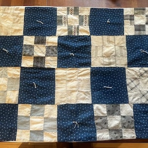 May include: A patchwork quilt with a grid pattern of alternating navy blue and cream-colored squares. Some squares feature a small white dot pattern, while others have patterned fabric. The quilt is handmade and has visible stitching.