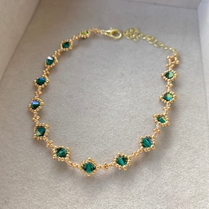 Op de afbeelding: Een delicate gouden ketting met smaragdgroene kristallen kralen. De ketting is gemaakt van kleine gouden kralen en heeft een eenvoudig ontwerp.
