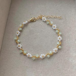 May include: A delicate gold chain bracelet with white and light green flower-shaped beads.
