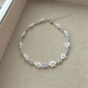 Puede incluir: Una delicada pulsera con cuentas blancas en forma de flor y pequeñas cuentas azul claro. La pulsera está ensartada en una cadena plateada y tiene un cierre ajustable. El diseño es simple y elegante, adecuado para el uso diario o ocasiones especiales.