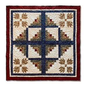 May include: A quilt with a log cabin pattern in shades of blue, green, and brown. The quilt is surrounded by a red border and features a white background.