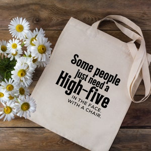 May include: A white canvas tote bag with black text that reads "Some people just need a High-five IN THE FACE. WITH A CHAIR."