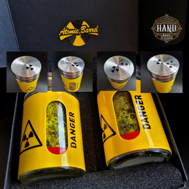 May include: Two yellow glass jars with black and white warning labels that say "DANGER" and a black and yellow radiation symbol. The jars have clear lids with a black radiation symbol. The jars are in a black box with a label that says "Atomic Barrel".