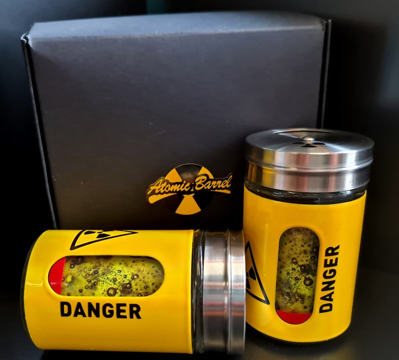 May include: Two yellow and black spice jars with silver lids. The jars have the words "DANGER" and "Atomic Barrel" printed on them.
