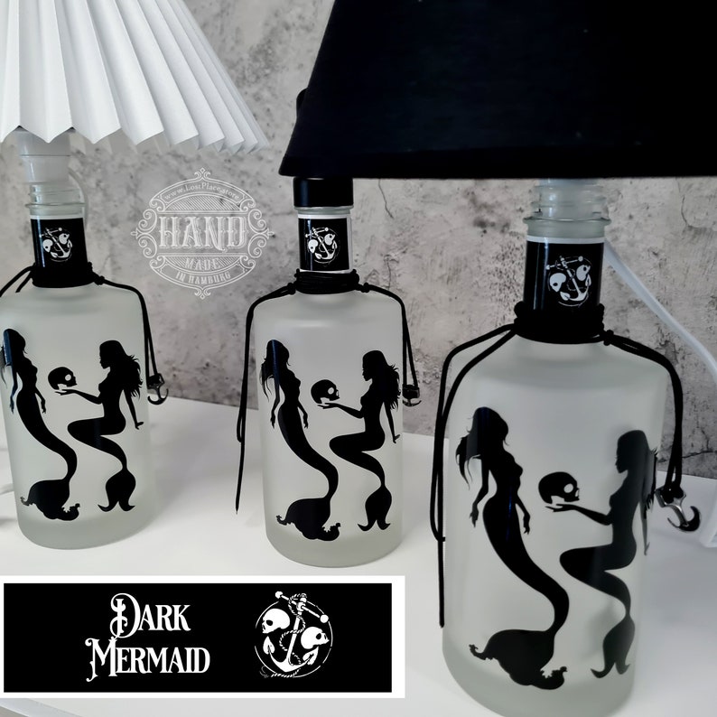 Op de afbeelding: Drie matglazen flessen met zwarte silhouetten van zeemeerminnen die schedels vasthouden. De flessen zijn versierd met zwart touw en een anker. De tekst "DARK MERMAID" staat op een zwart label met een wit anker en schedels.
