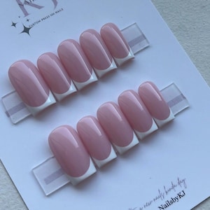 May include: Two sets of custom press-on nails with a classic French manicure design. Each nail is a soft pink with a white tip. The nails are displayed on a white card with text that reads "Custom Press On Nails" and "NailsbyKJ".
