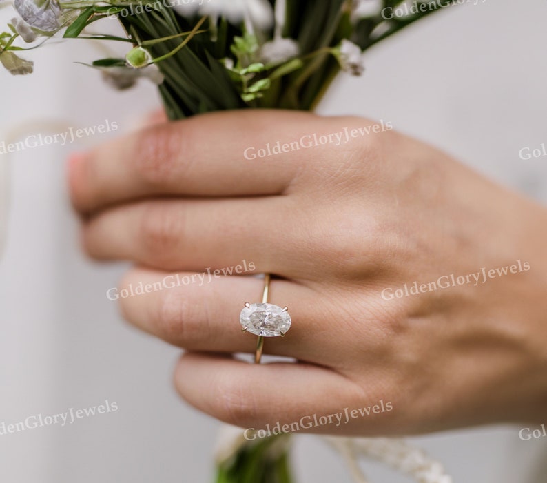 Puede incluir: Primer plano de una mano con un anillo de oro con un diamante de forma ovalada.