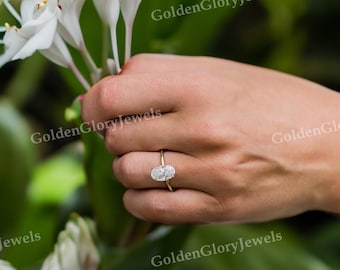 May include: A close-up of a hand wearing a gold ring with an oval-shaped diamond. The ring is set in a simple band and the diamond is sparkling.