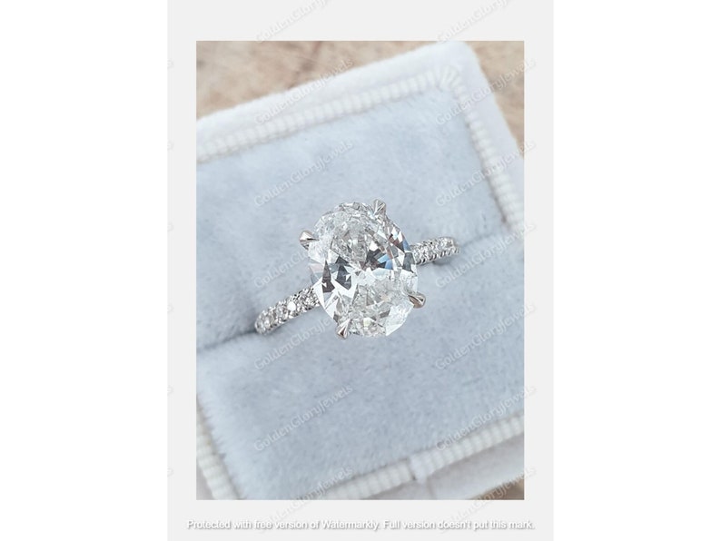 Op de afbeelding: Een zilveren verlovingsring met een grote ovale diamant en kleinere diamanten die in een pav&eacute;-band zijn gezet.