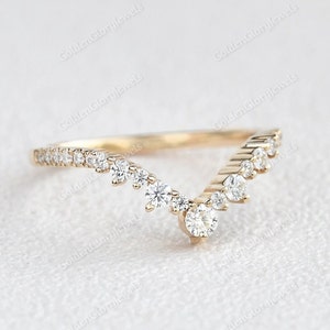 May include: A delicate gold band ring with a V-shaped design featuring a row of small diamonds on each side and a larger diamond at the point of the V.