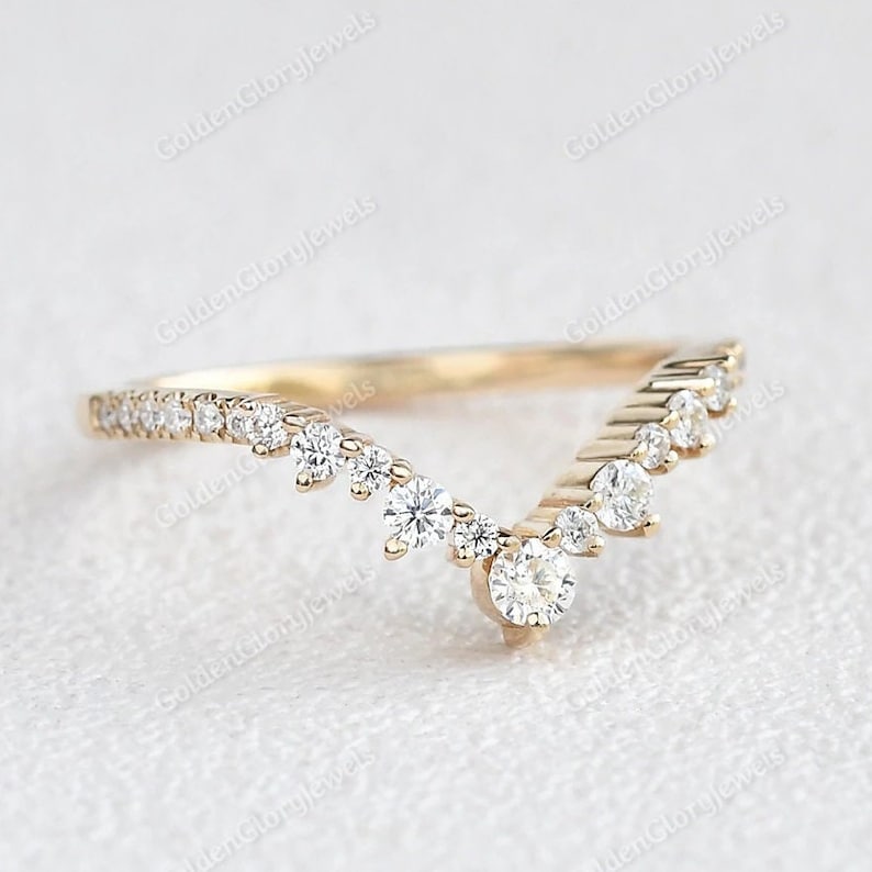 May include: A delicate gold band ring with a V-shaped design featuring a row of small diamonds on each side and a larger diamond at the point of the V.