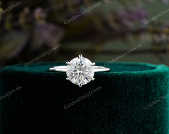 May include: A solitaire engagement ring with a large, round, brilliant-cut diamond set in a white gold band. The ring is displayed on a green velvet box.