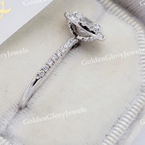 Op de afbeelding: Een zilveren ring met een peervormige diamant in het midden, omringd door een halo van kleinere diamanten. De band is ook bezet met kleinere diamanten.