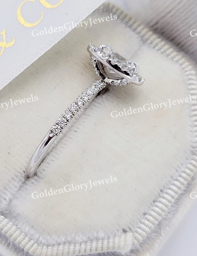Op de afbeelding: Een zilveren ring met een peervormige diamant in het midden, omringd door een halo van kleinere diamanten. De band is ook bezet met kleinere diamanten.