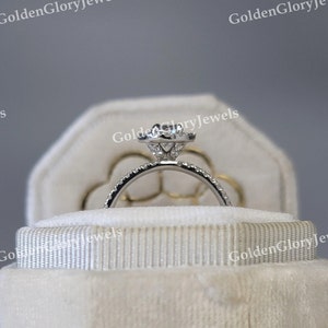 Op de afbeelding: Een witte fluwelen ringendoos met een zilveren verlovingsring met een grote centrale diamant en kleinere diamanten eromheen.