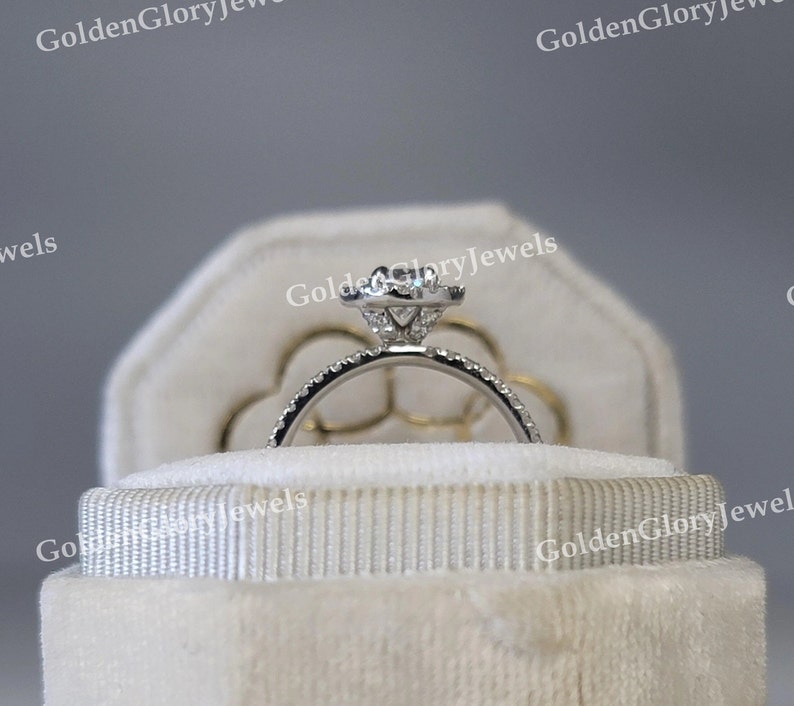 Op de afbeelding: Een witte fluwelen ringendoos met een zilveren verlovingsring met een grote centrale diamant en kleinere diamanten eromheen.