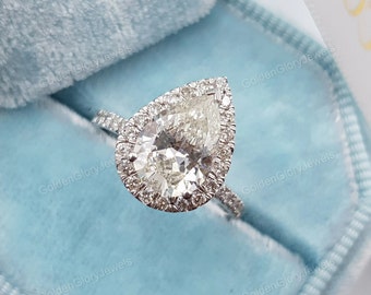 May include: A pear-shaped diamond engagement ring with a halo setting. The ring is set in white gold and features a large, clear diamond in the center.