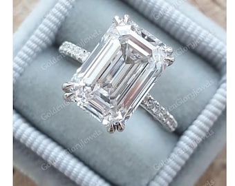 May include: A silver ring with a large, clear emerald-cut diamond. The diamond is set in a pave setting with smaller diamonds on the band.