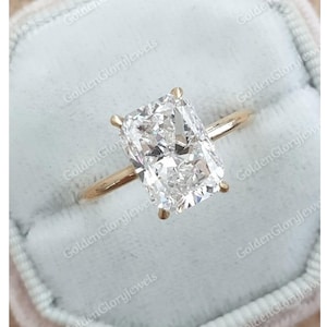 以下が含まれることがあります： 大きな透明なクッションカットのダイヤモンドがついた金の婚約指輪です。