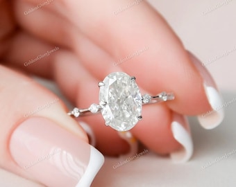 May include: A silver engagement ring with an oval-shaped diamond. The ring has a delicate band with small diamonds on either side of the center stone.