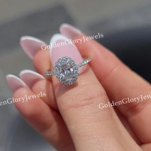 Op de afbeelding: Een zilveren ring met een grote ovale diamant omgeven door een halo van kleinere diamanten. De ring is gezet op een dunne band.
