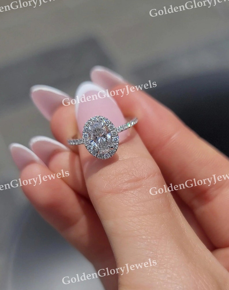 Op de afbeelding: Een zilveren ring met een grote ovale diamant omgeven door een halo van kleinere diamanten. De ring is gezet op een dunne band.