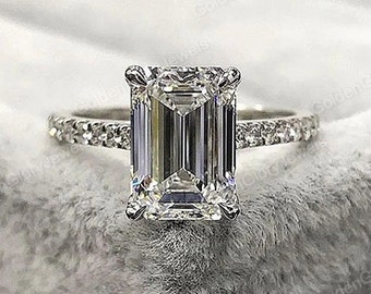 Puede incluir: Un anillo de compromiso de plata con una gran piedra central de diamante de talla esmeralda y una banda pavé de diamantes.