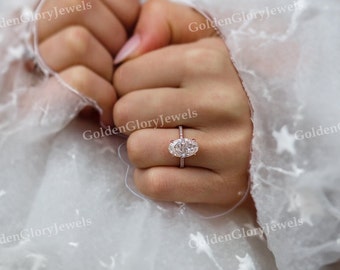 May include: A close-up of a hand wearing a rose gold engagement ring with an oval-shaped diamond. The ring has a pave setting with smaller diamonds around the center stone.