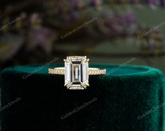 May include: A gold engagement ring with a large emerald cut diamond. The ring has a thin band with small diamonds set in a pave setting.