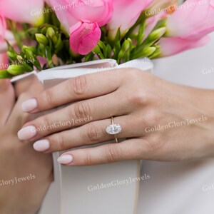 Puede incluir: Primer plano de una mano con un anillo de oro con un gran diamante de forma ovalada. El anillo est&aacute; engastado en una banda sencilla.