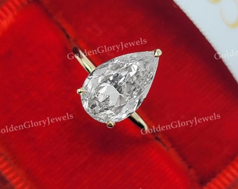 May include: A pear-shaped diamond engagement ring set in a yellow gold band. The ring is displayed in a red velvet ring box.